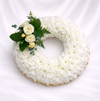 Round funeral wreath of white chrysanthemums with cream roses and greenery accent, displayed on a soft white and grey silk background