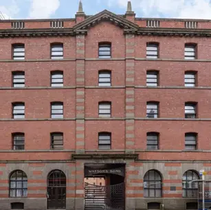 Historic red-brick warehouse facade with many windows, Watson's Bond over the entrance, and scaffolding beside it.