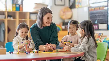 Teacher sits at a table with students, working on an activity