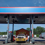 White truck with wide load sign and pulling prebuilt log cabin at the gas pump.