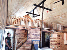 A loft with wooden rails beneath a cathedral ceiling with dark wood beams.