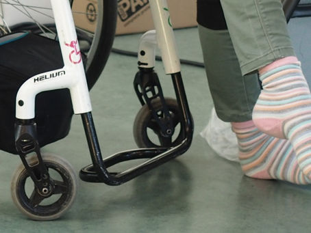 A close up of a manual wheelchair, the person is wiggling their socked feet to help their PoTS