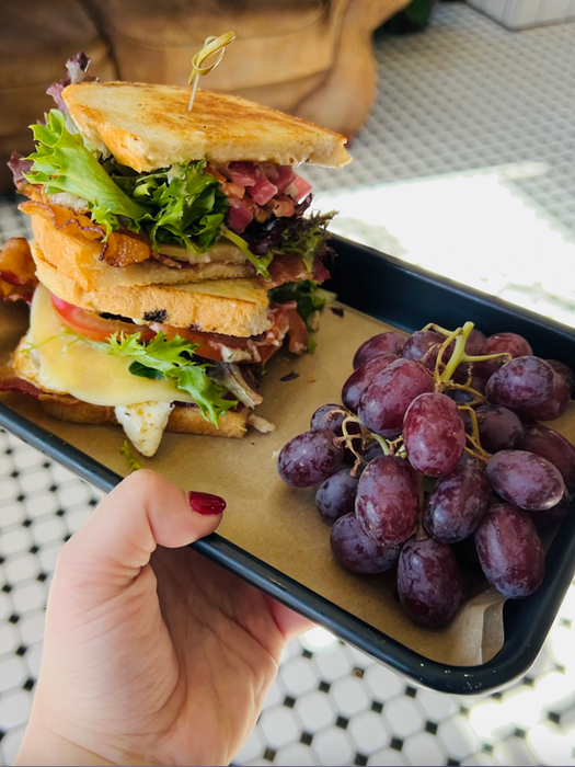 Delicious sandwich with bacon, egg, lettuce, and grapes on a tray
