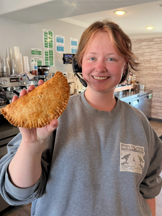 Girl with drive-thru headset on holding a hand pie in her right hand and smiling at the camera.