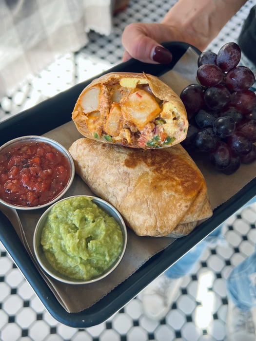 Tray of food holding a burrito, salsa, guacamole, and grapes.