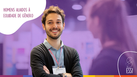 Imagem artística com fundo roxo claro, logotipo da Éssi Consultoria no canto inferior direito e título do artigo no canto superior esquerdo, com letras na cor roxa sob recorte orgânico branco. Fotografia em primeiro plano de um homem, branco, barba curta, cabelos castanhos, olhando para a lateral. No lado direito, em desfoque, é possível notar a presença de uma mulher de costas para a câmera e olhando na direção do homem. Ela também sorri. Ao fundo, o cenário desfocado indica um escritório.