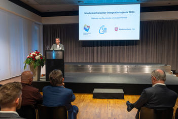 Mann am Rednerpult hält Rede vor der Bühne. Wiederstädtischer Integrationspreis 2024.