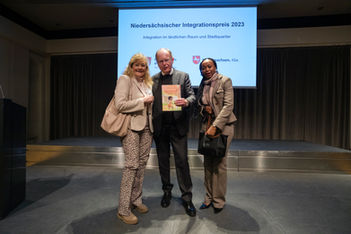 Drei Personen auf einer Bühne, Niedersächsischer Integrationspreis 2023 im Hintergrund