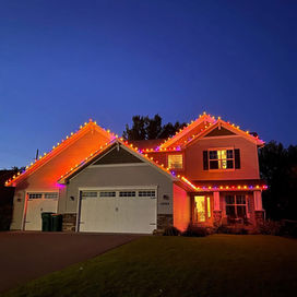House with orange holiday lights against dark blue sky. Home Aglow Holiday L.