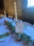 Paxton, Illinois wedding rental showing guest table with faux greenery garland running down the middles, brass candlesticks with taper candles and table number "9" sign displayed on wood slice table number holder.