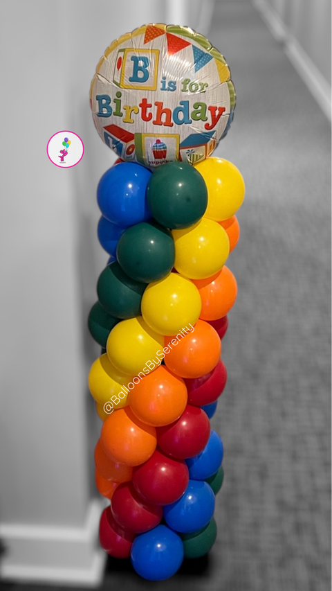 Rainbow Spiral Column with stacked balloons in red, orange, yellow, green, blue, and teal, topped by a foil balloon that reads “B is for Birthday.”