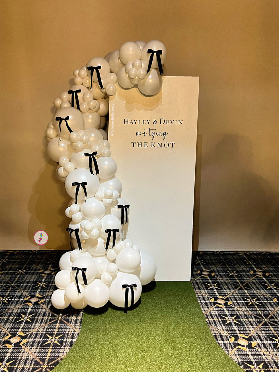 Custom engagement party balloon backdrop with pearl white balloons, black bows, and Hayley and Devin tying the knot backdrop panel.