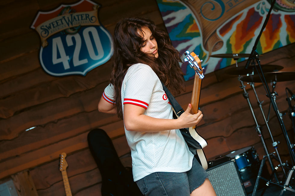 Musician in a white shirt plays electric guitar on stage, wooden backdrop with colorful signs. Energetic mood, instruments visible.