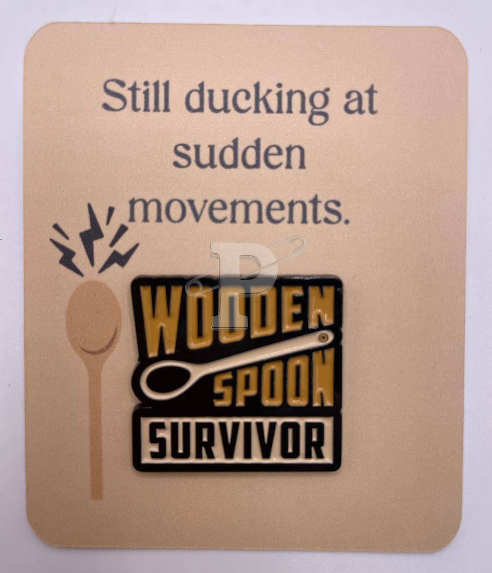 A flat card that says still ducking at sudden movements with attached pin that says "Wooden Spoon Survivor"
