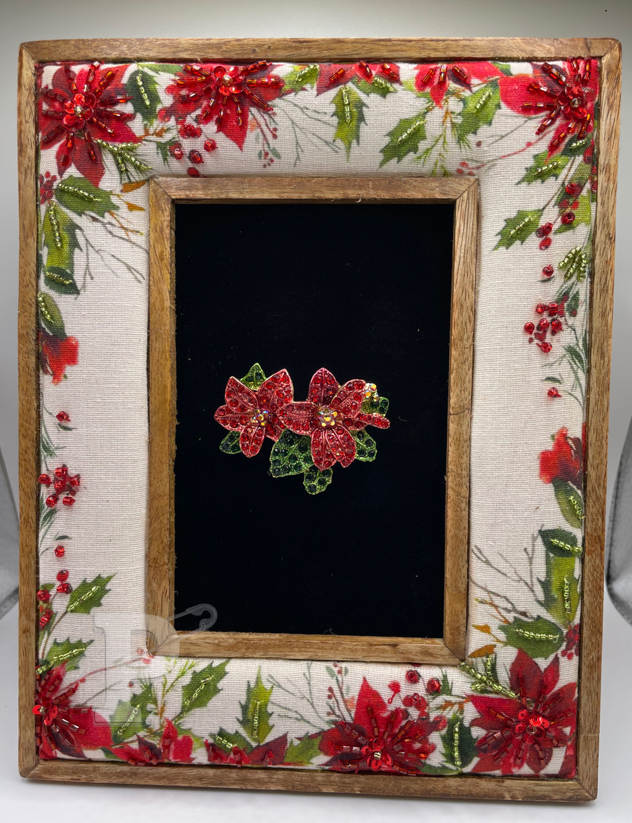 Christmas brooch art featuring poinsettia pin in decorative fabric frame.