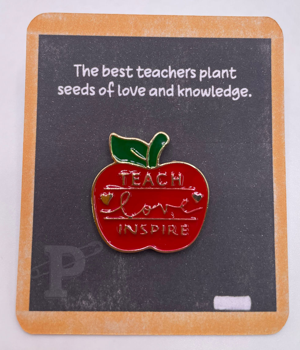 Pin card with apple enamel pin that reads, “Teach love inspire,” on a chalkboard-style background