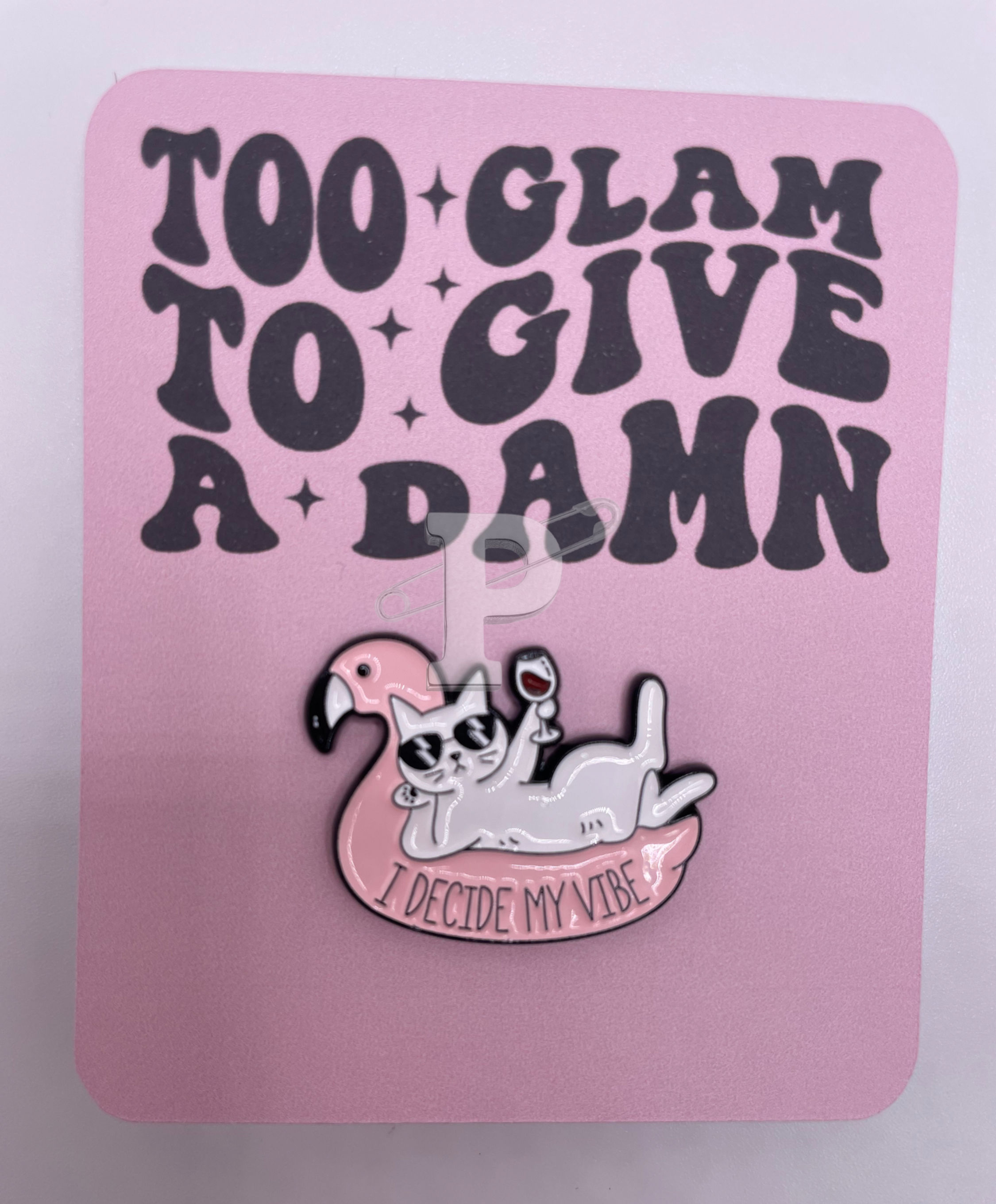 A flat card that says "Too glam to give a damn" with a cat in a flamingo floatie pin that reads "I decide my vibe"