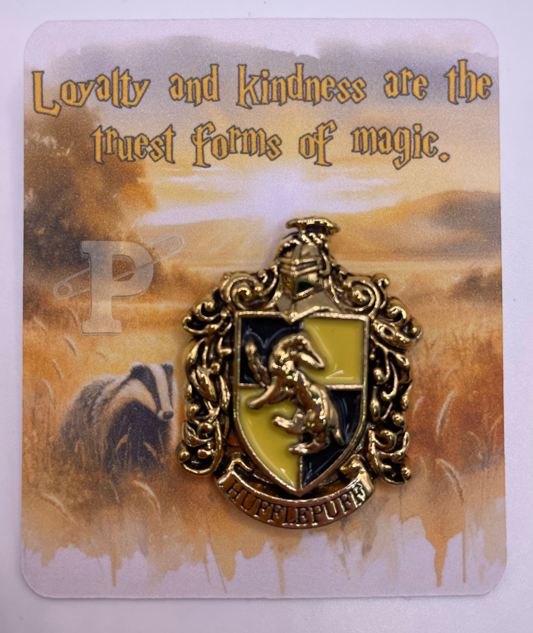 Hufflepuff crest brooch on a flat card with golden fields that reads “Loyalty and kindness are the truest forms of magic"