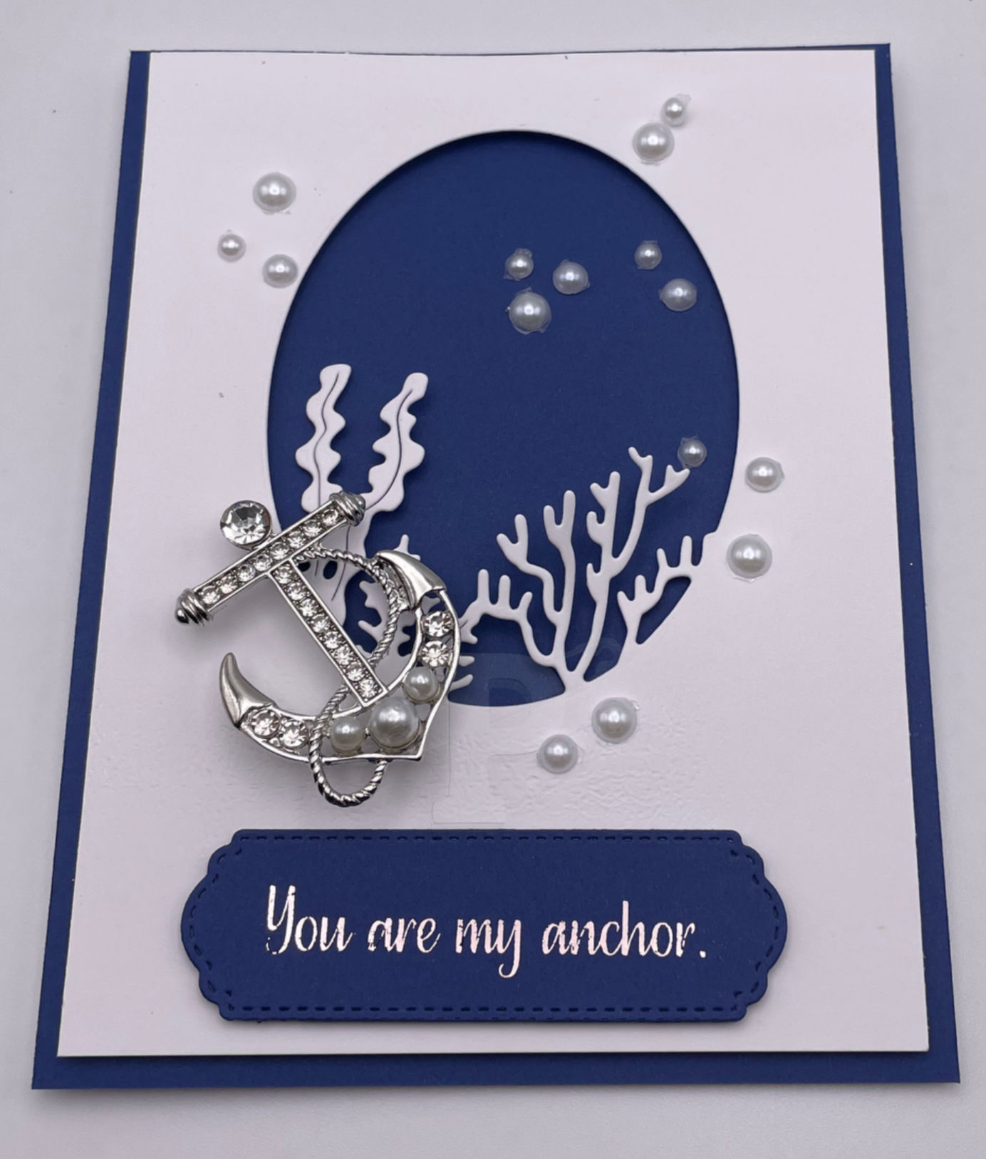 Greeting card with silver anchor brooch with pearls on ocean background; symbolizes strength and support.