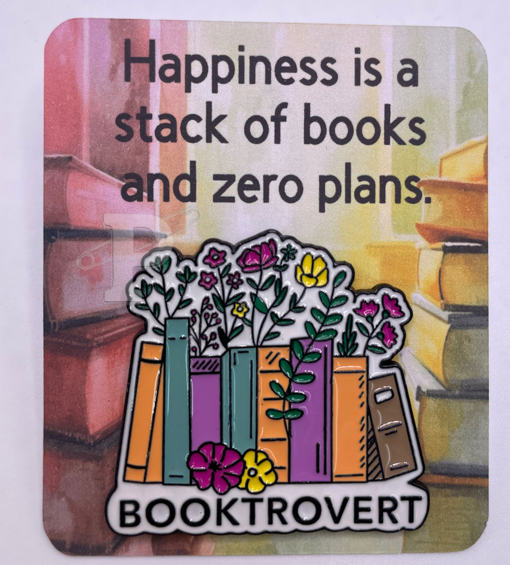 Flat card that reads “Happiness is a stack of books and zero plans” with pin that reads “Booktrovert.”