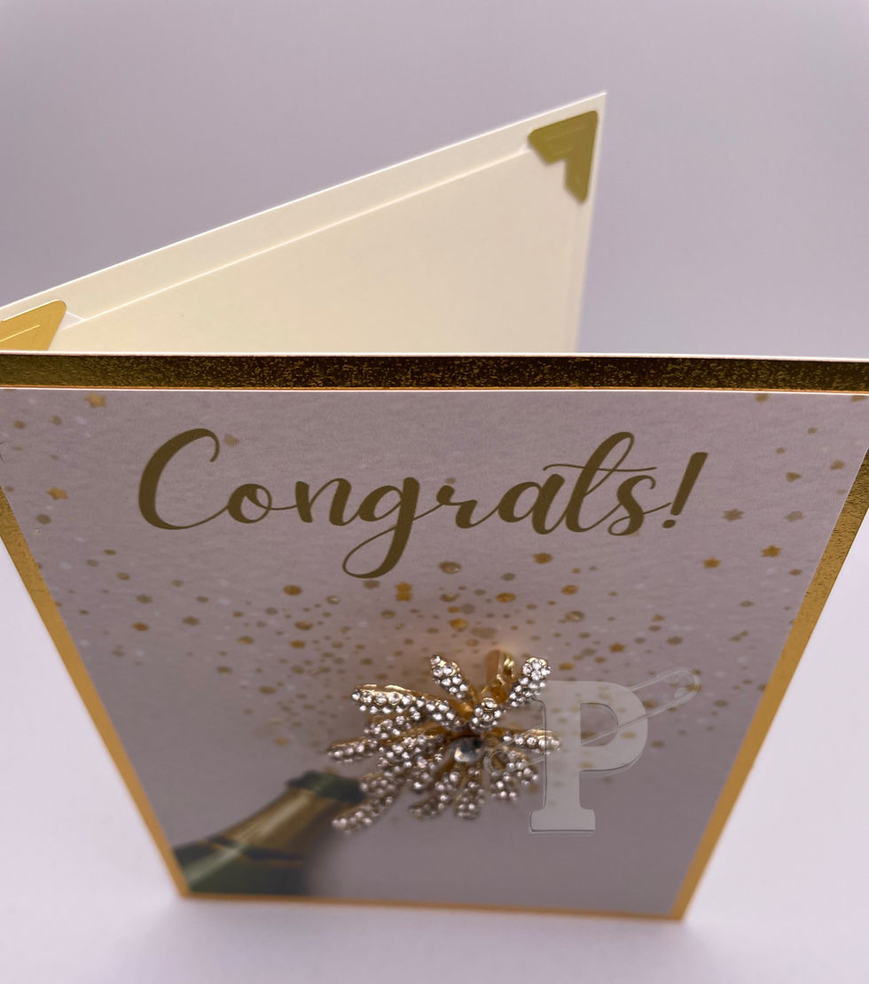 Top view of greeting card that reads “Congrats!” with champagne bottle and sparkling firework brooch.