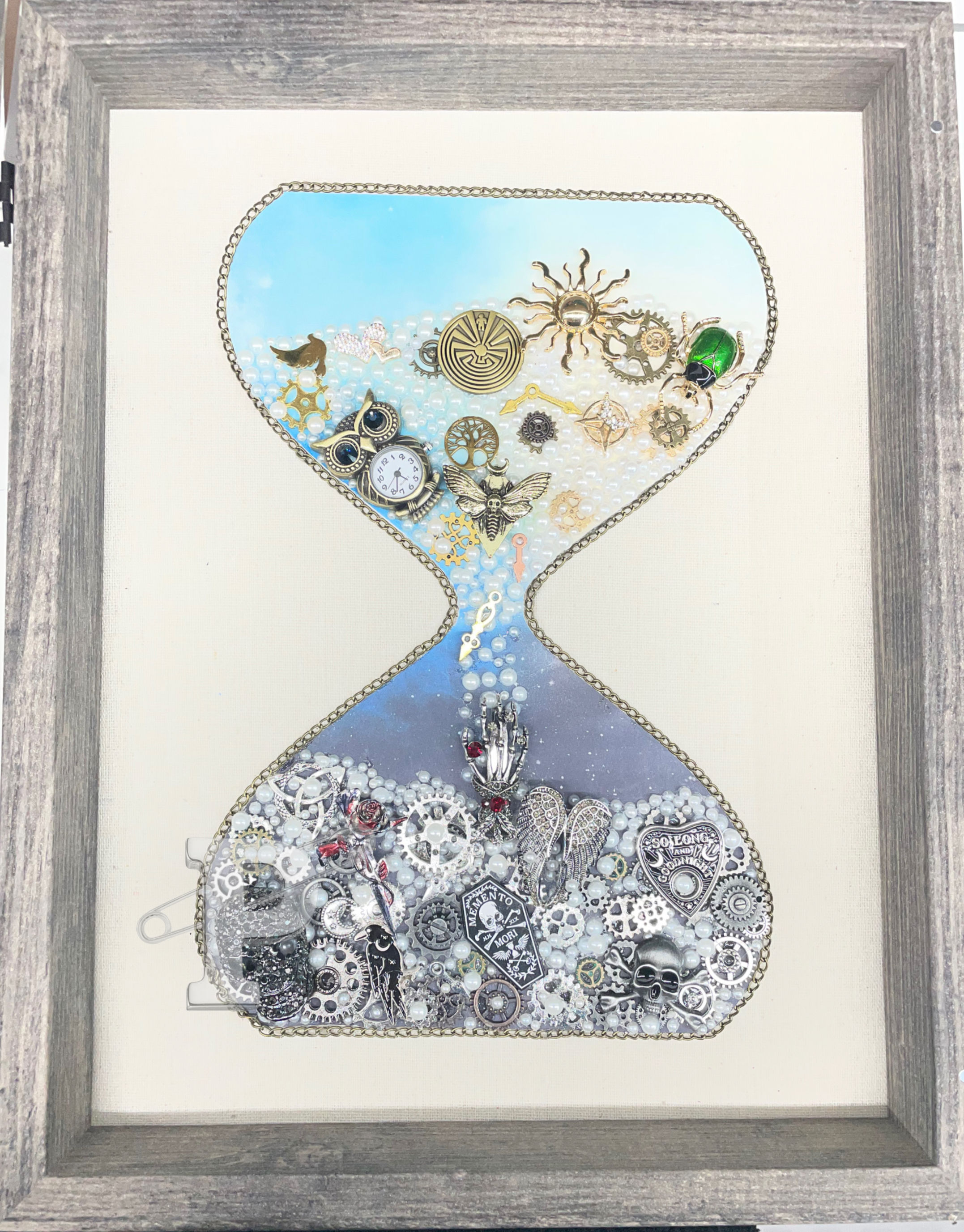 Framed hourglass mixed media art with gears, pearls, clocks, wings, skulls, and celestial charms