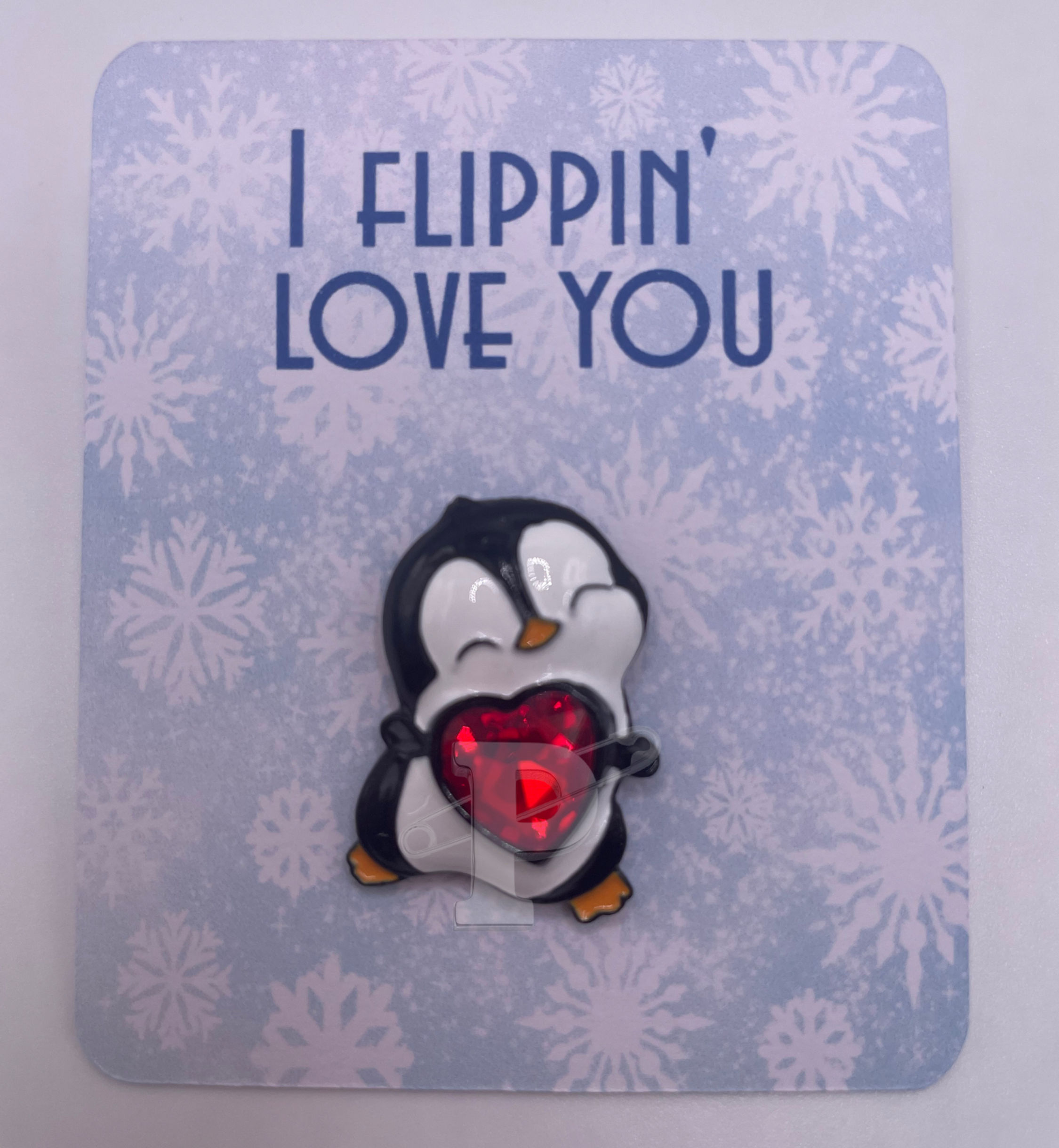 A flat card that reads "I flipping love you" with a penguin holding a heart pin attached"