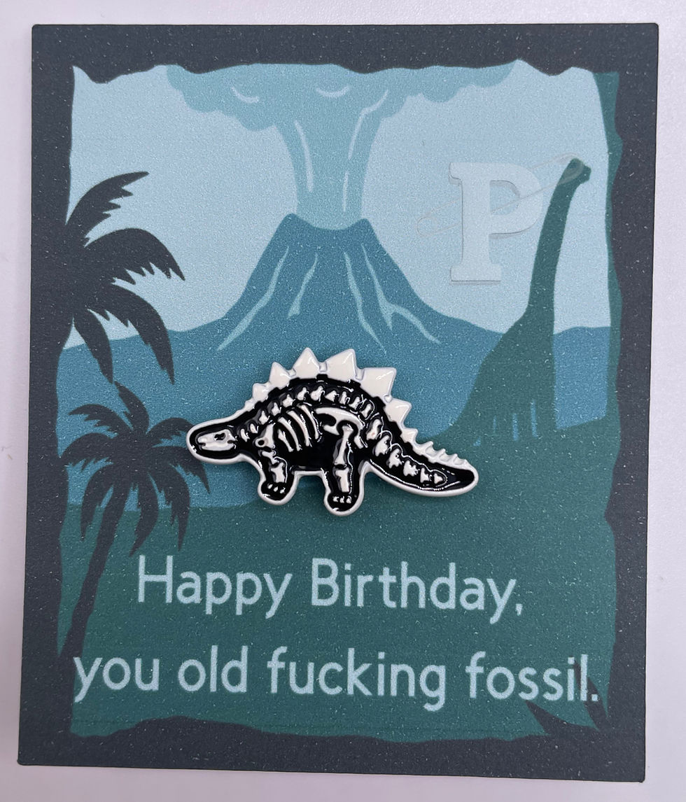 Flat card that reads “Happy Birthday, you old fucking fossil.” with dinosaur skeleton lapel pin.