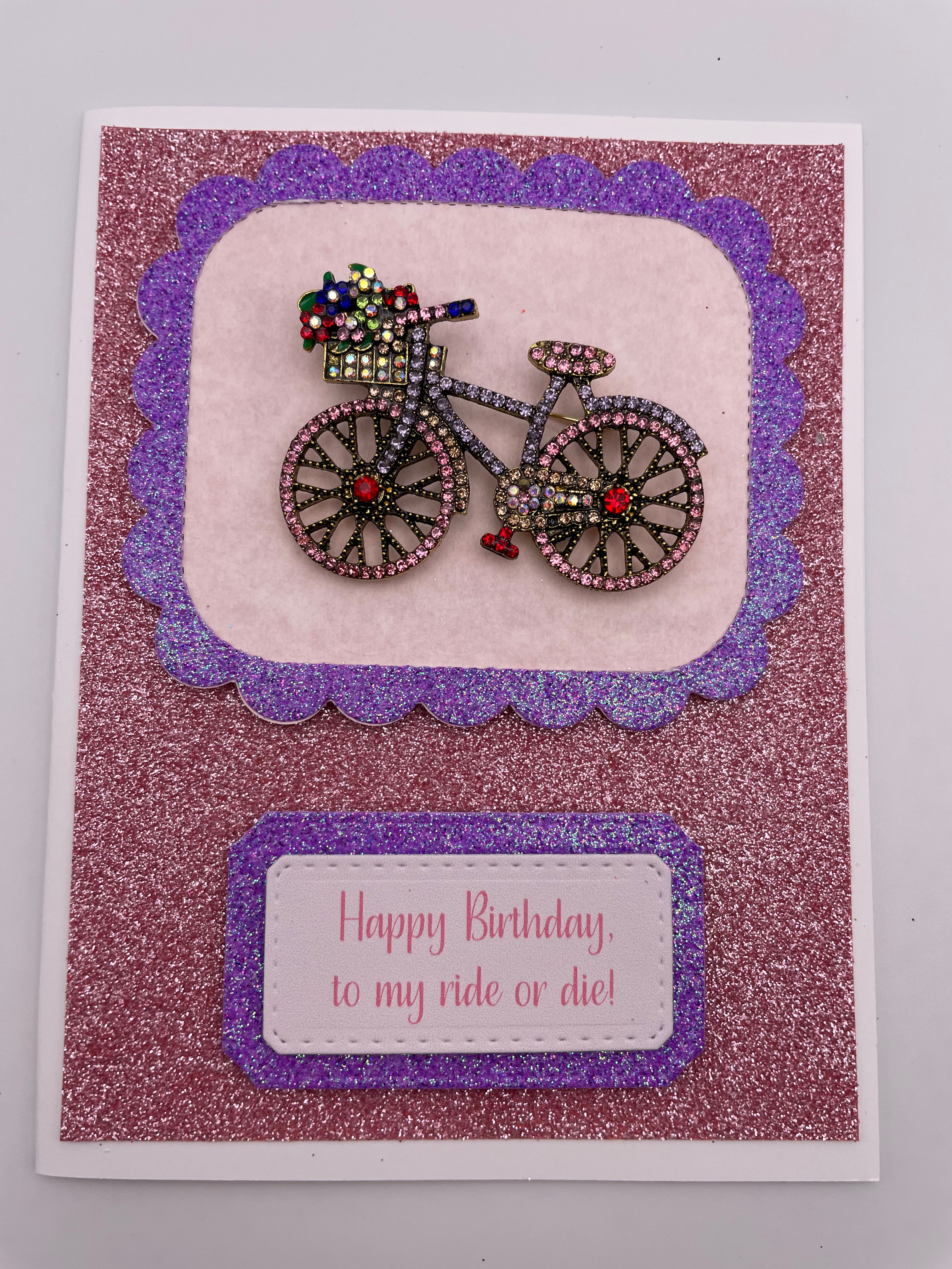 Colorful rhinestone bicycle brooch on glittery background birthday card with ‘Ride or Die’ sentiment.”