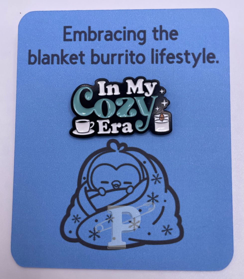 A flat card that reads "Embracing the blanket burrito lifestyle with an "In my cozy era" pin attached.