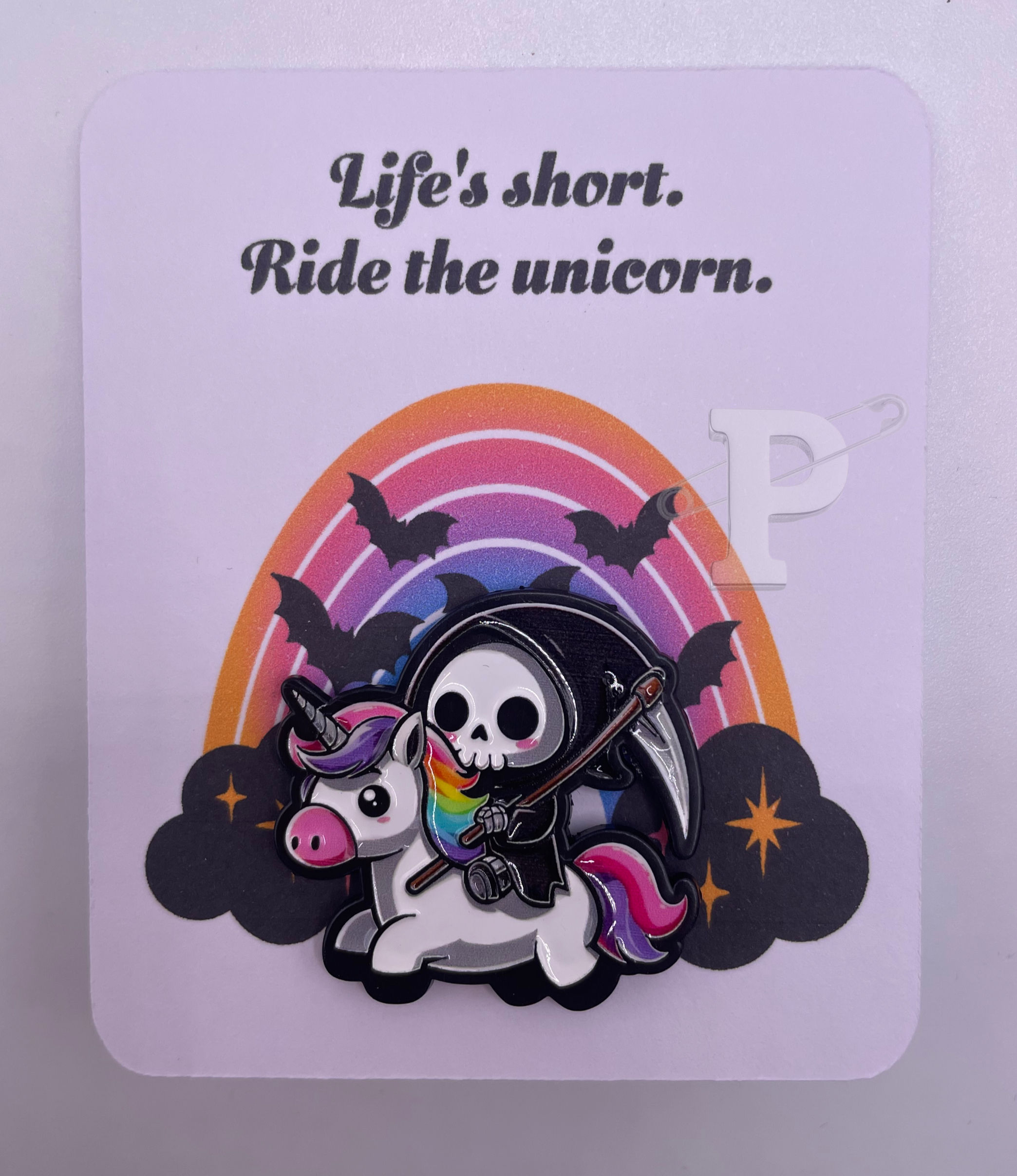 flat card that reads ‘life’s short ride the unicorn’ with enamel pin featuring grim reaper riding a unicorn