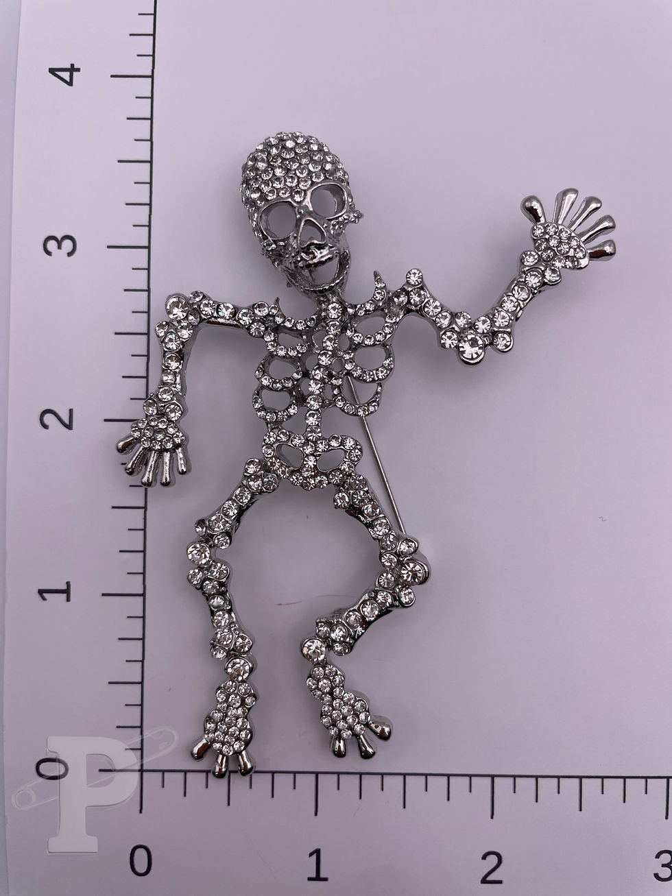 Thumbnail: Silver-tone skeleton brooch embellished with sparkling clear crystal rhinestones shown with ruler for size reference.