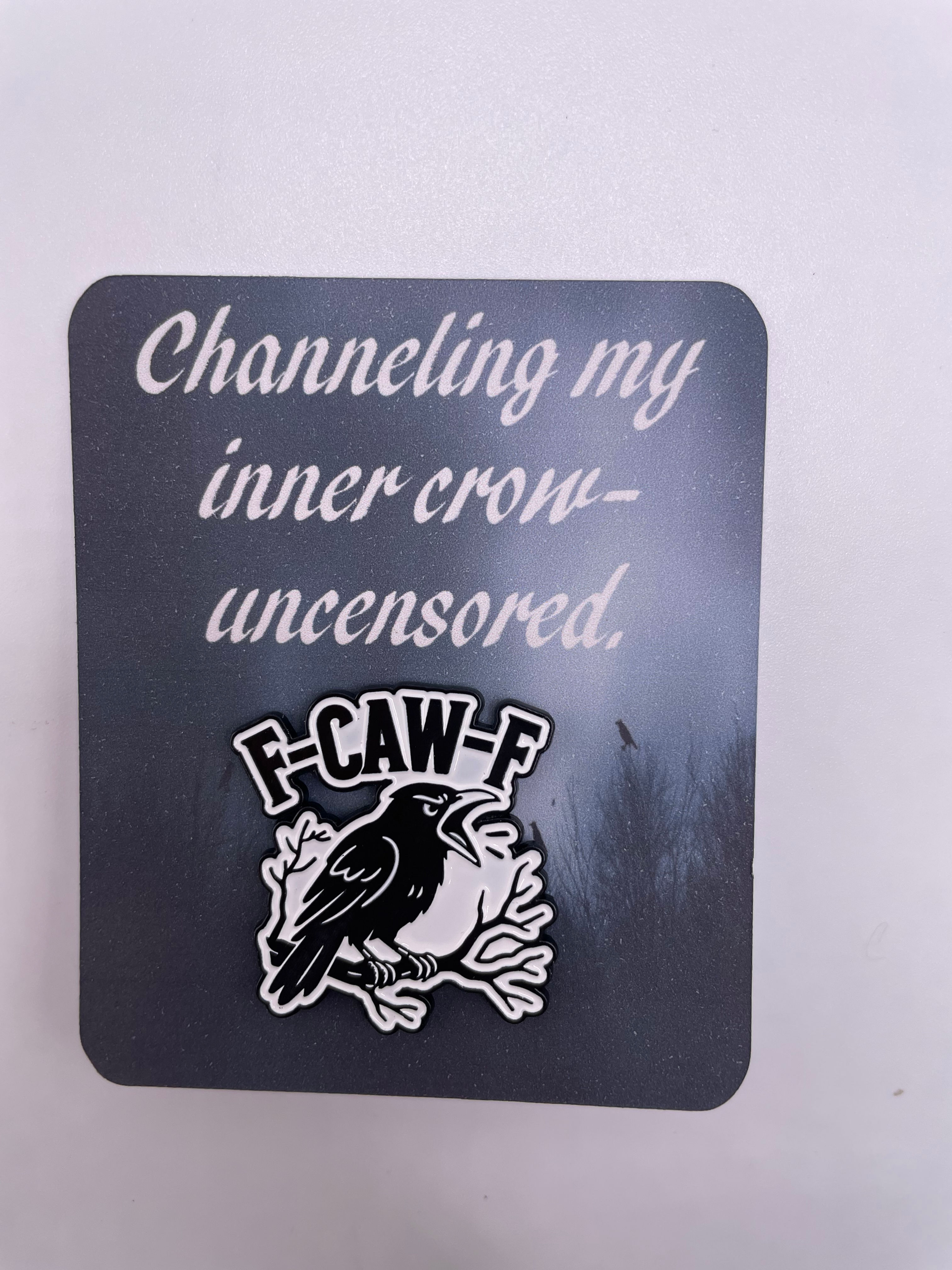Flat pin card with black and white crow pin that reads “F-CAW-F” and the caption, “Channeling my inner crow — uncensored.”