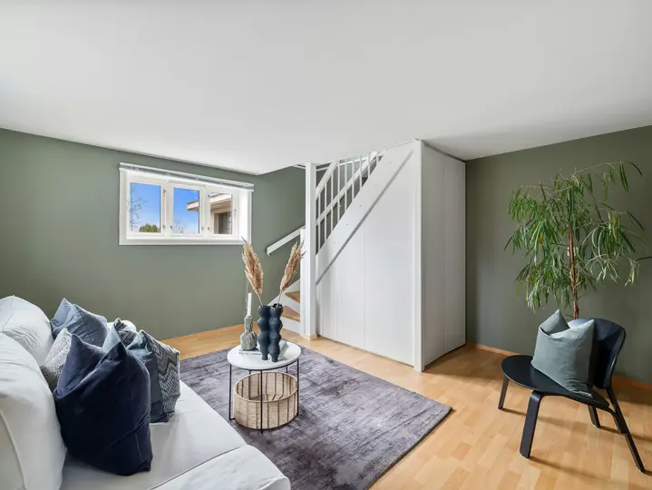 A modern living room with green walls, a white sofa adorned with blue and gray pillows, and a black accent chair with a green pillow.webp