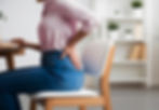 Woman sitting on a chair holding her lower back in pain, illustrating symptoms of degenerative disc disease that can be treated with non-surgical spinal decompression in Cary, NC.