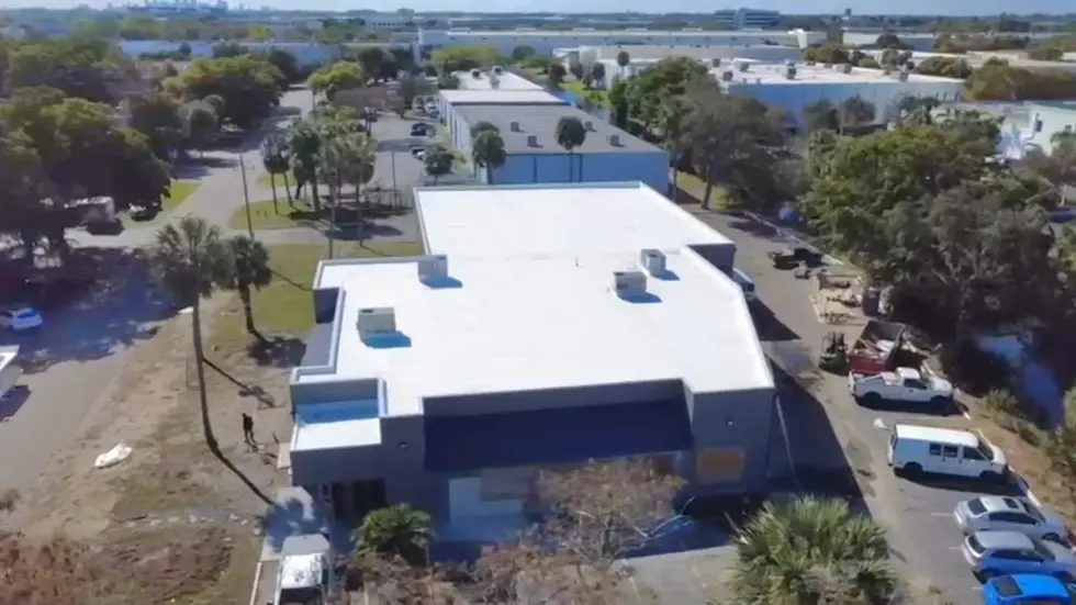 Drone view from above showing the front and roof of a commercial property with a white flat roof, HVAC units, and surrounding streets and parking lots