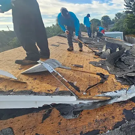 Roofing team tearing off damaged shingles and underlayment during a full roof replacemen.w