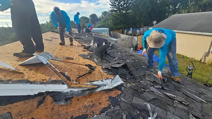 Roofers clearing old roofing materials and flashing from a sloped residential roof.webp