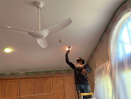 painter on a ladder uses a brush to apply fresh paint around the lights in the sunroom ceiling in Briar Chapel, Chapel Hill