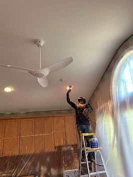 painter on a ladder uses a brush to apply fresh paint around the lights in the sunroom ceiling in Briar Chapel, Chapel Hill