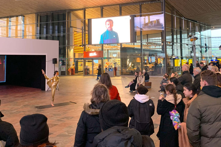 Yoga performance art as part of IFFR. Unfolding is a video installation by Anne Fehres and Luke Conroy at Rotterdam Central Station during IFFR 2024. The video installation features a golden figure doing yoga moves, set in the year 2070. The installation premiered as part of the International FIlm Festival Rotterdam and Art Rotterdam, as part of the Art Directions program. The year is 2070 and you are about to be catapulted into an absurd, yet eerily plausible yoga session. Through an odyssey that transcends the bounds of conventional cinema, a captivating experiment unfolds, one that plunges its participants into profound contemplations on the interplay between humanity, nature and the wellness industry.