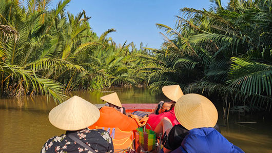 Travelers relaxing on colorful bean bags during quiet boat trip through secluded Mekong Delta canal, Half-Day Tour in Ben Tre