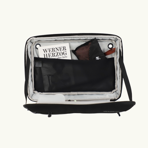 Open black travel bag showing Werner Herzog book and other items
