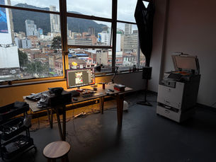 Vista interior del taller multidisciplinar grama/naipe en Talleres Telecom, mostrando mesas de trabajo, equipos y grandes ventanales con vista a la ciudad de Bogotá.