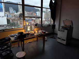 Vista interior del taller multidisciplinar grama/naipe en Talleres Telecom, mostrando mesas de trabajo, equipos y grandes ventanales con vista a la ciudad de Bogotá.