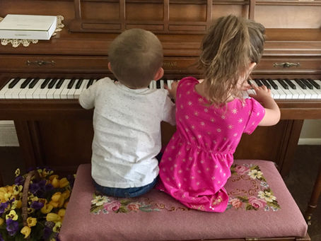 two children playing the piano. artificial flowers in the background.