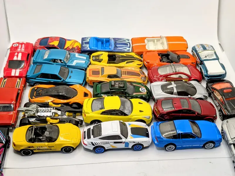 Assorted colorful toy cars arranged in rows on a white surface, featuring red, blue, orange, and yellow vehicles.