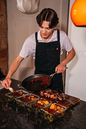 Chef Jaxon Narramore spooning food from a pan into a glass container as he prepares a meal