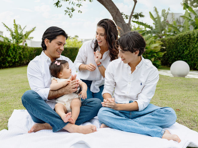 Family of four sitting together in a garden during a first birthday photoshoot in Barbados, with parents and son gathered around their baby girl who just turned one.