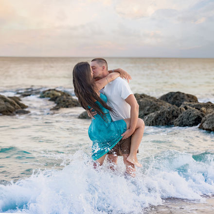 Man holding his partner by the leg while standing together in the ocean during a playful and romantic couples photoshoot in Barbados.